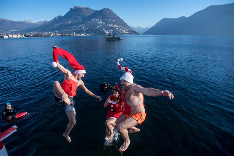 Varias personas luciendo gorros navideños participan en el tradicional baño de invierno en el lago Lugano en Paradiso (Suiza).