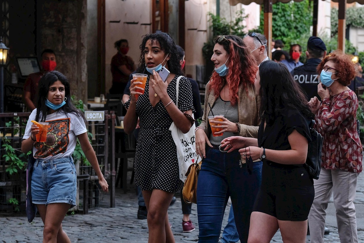  Mujeres jóvenes con mascarillas protectoras caminan en la Piazza di San Calisto en el distrito de Trastevere en Roma, Italia.