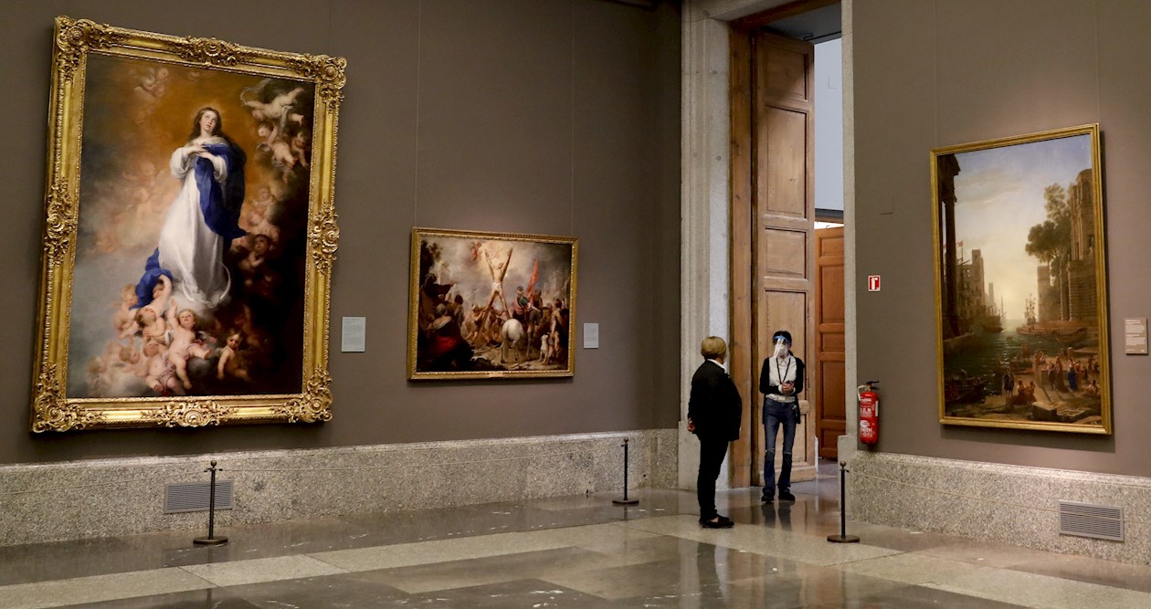 Dos empleadas del Museo del Prado con máscarillas y pantallas protectoras junto a la obra "La Inmaculada Concepción de los Venerables" (i),de Bartolomé Esteban Murillo, durante la presentación de "Reencuentro".
