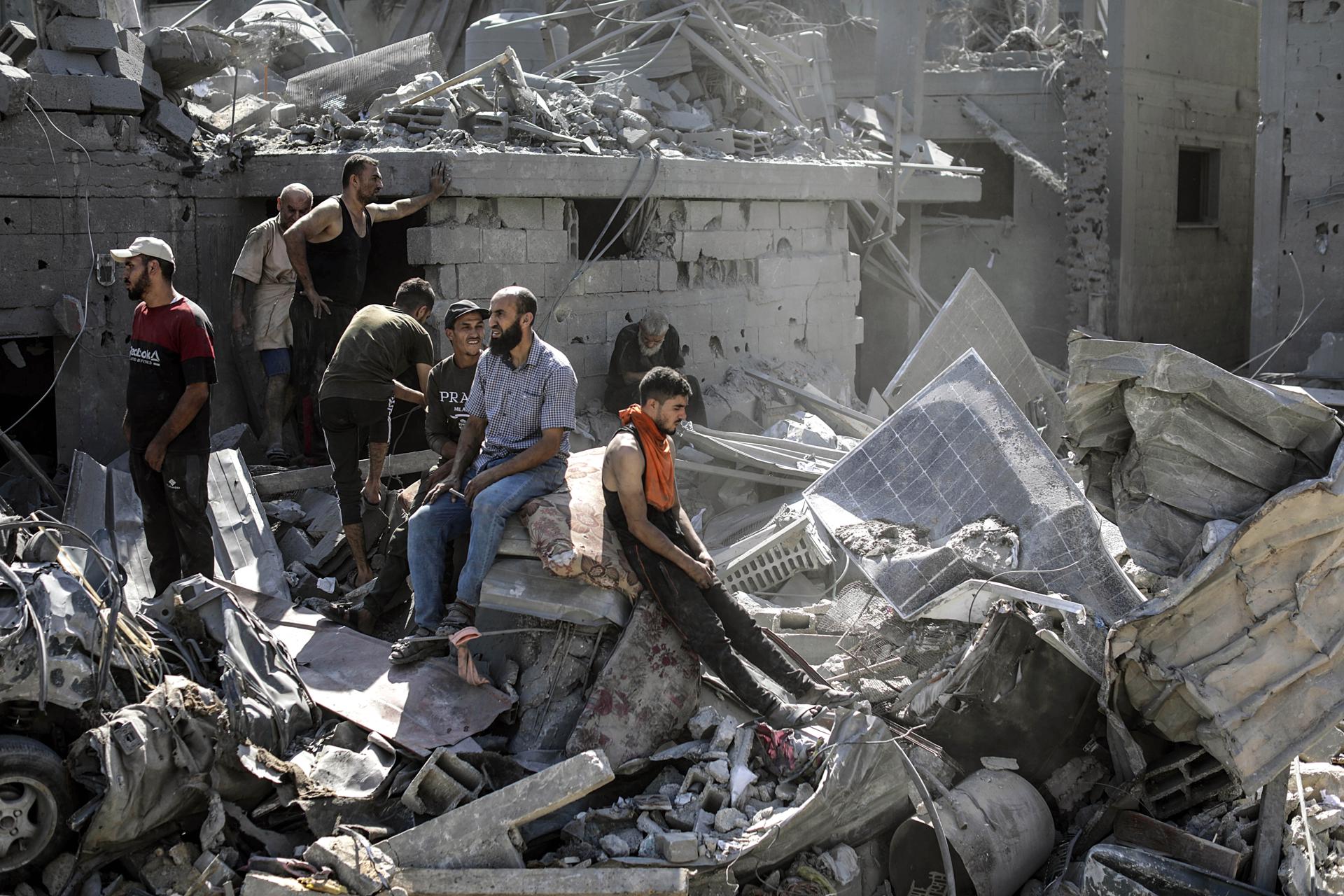Palestinos sentados entre los escombros de un edificio residencial derribado por un ataque aéreo israelí.