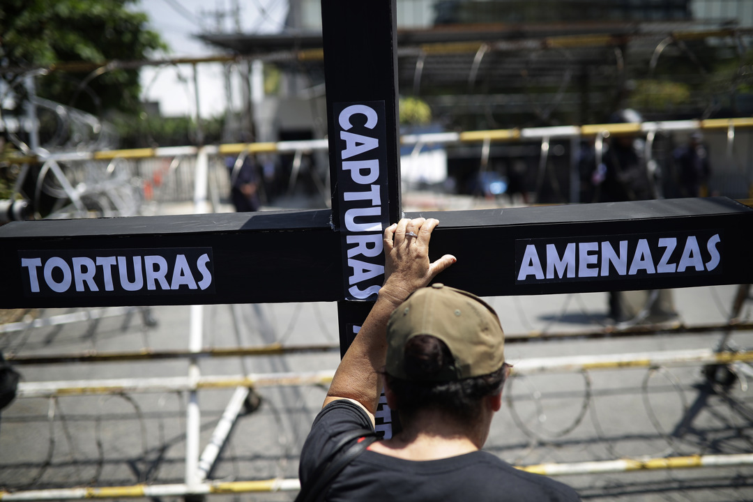 Una persona sostiene una cruz con las palabras escritas "torturas, amenazas, capturas arbitrarias".
