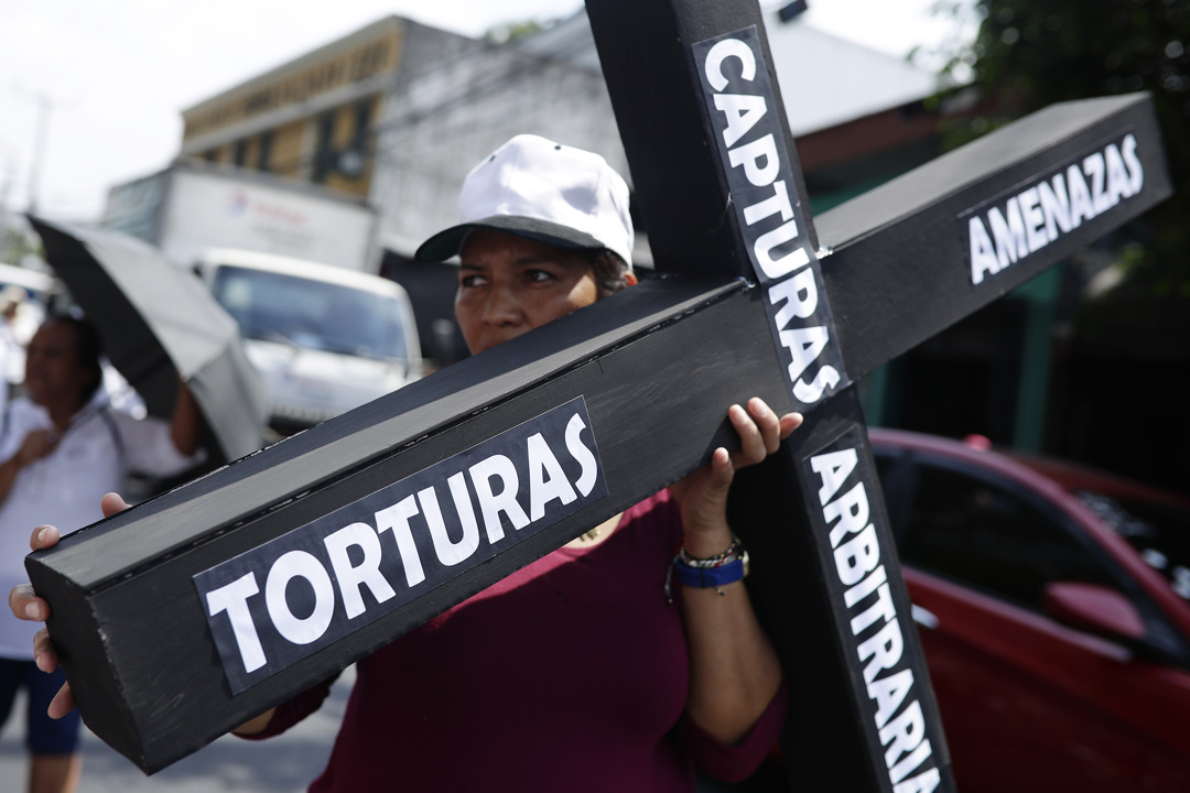 Una persona sostiene una cruz con las palabras escritas "torturas, amenazas, capturas arbitrarias" durante la marcha.