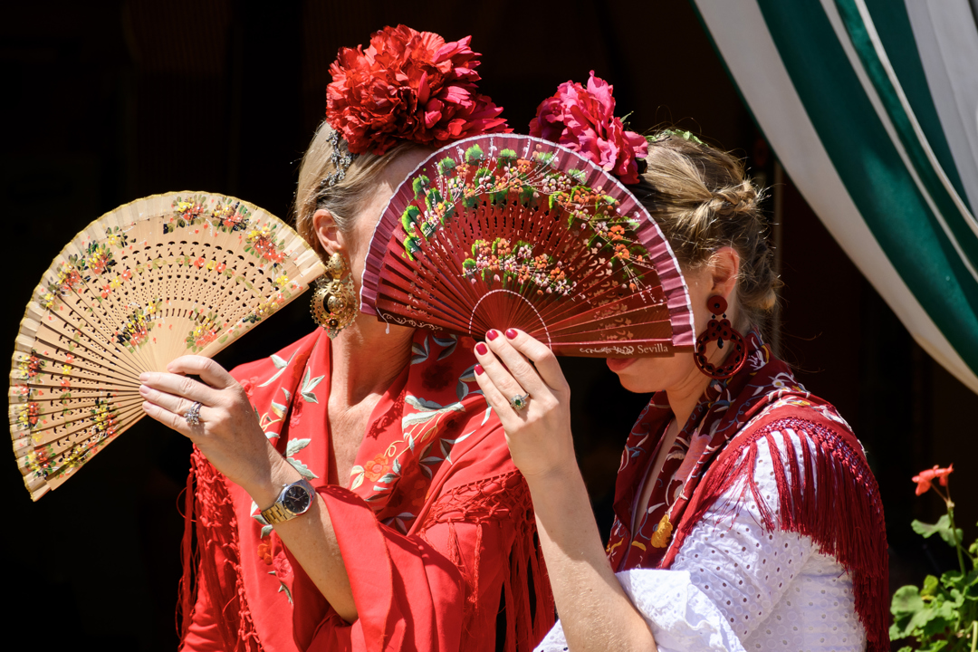 Dos mujeres vestidas de flamenca se protegen del sol durante la feria.