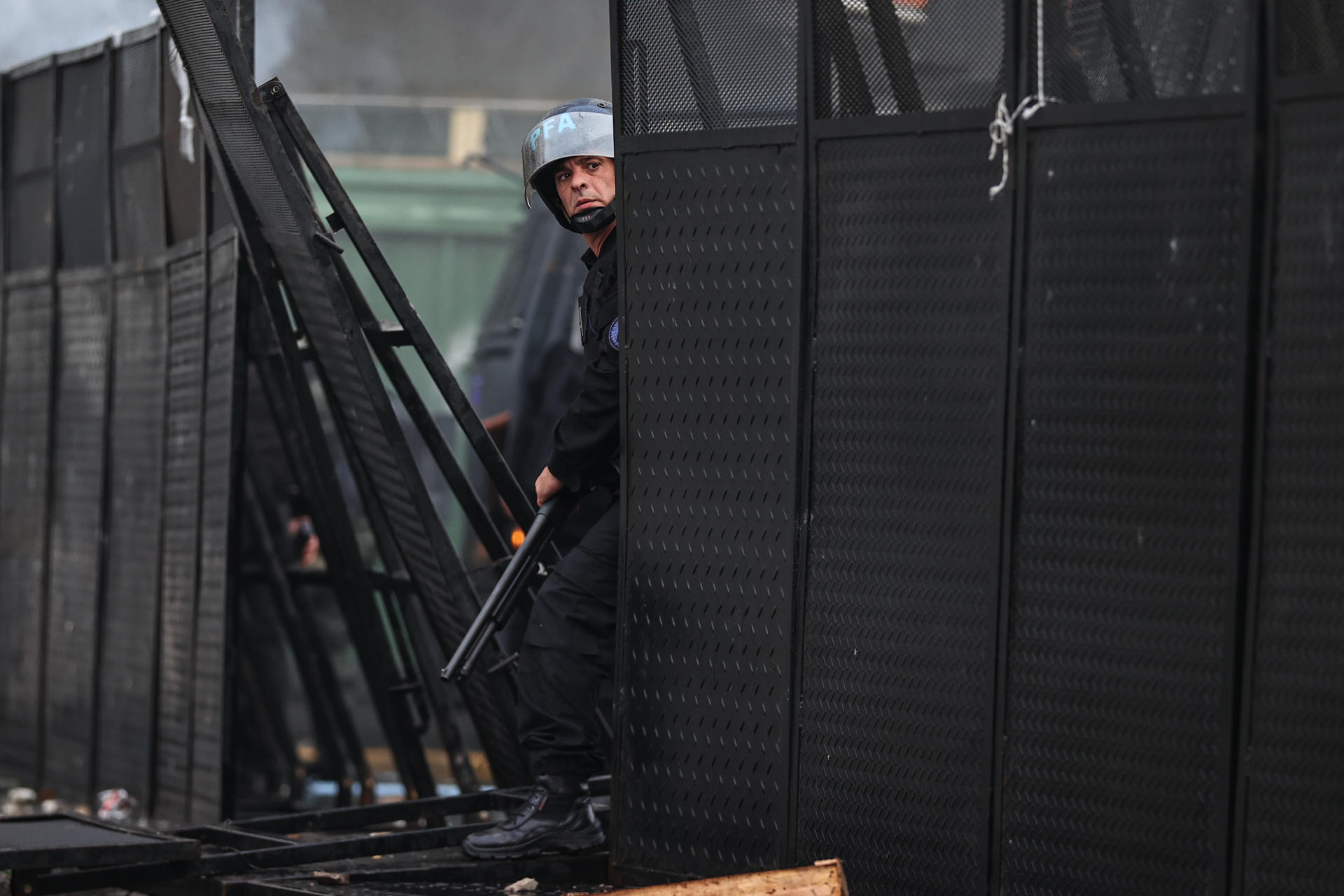 Un policía se resguarda tras unas rejas durante enfrentamientos.