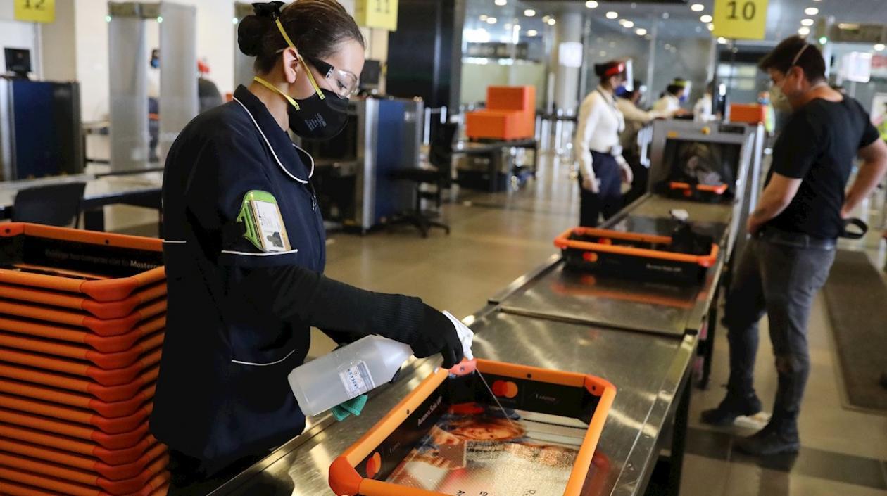 Una trabajadora desinfecta uno de los recipientes de objetos personales utilizados durante los controles de seguridad previos al abordaje, en el Aeropuerto Internacional El Dorado, en Bogotá.