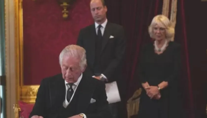 Carlos III firma el documento luego de juramentarse. A su lado la reina consorte, Camila, y el príncipe de Gales, Guillermo.