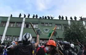 Policías bolivianos saludan desde el techo de una unidad policial a ciudadanos apostados en las puertas de la misma.
