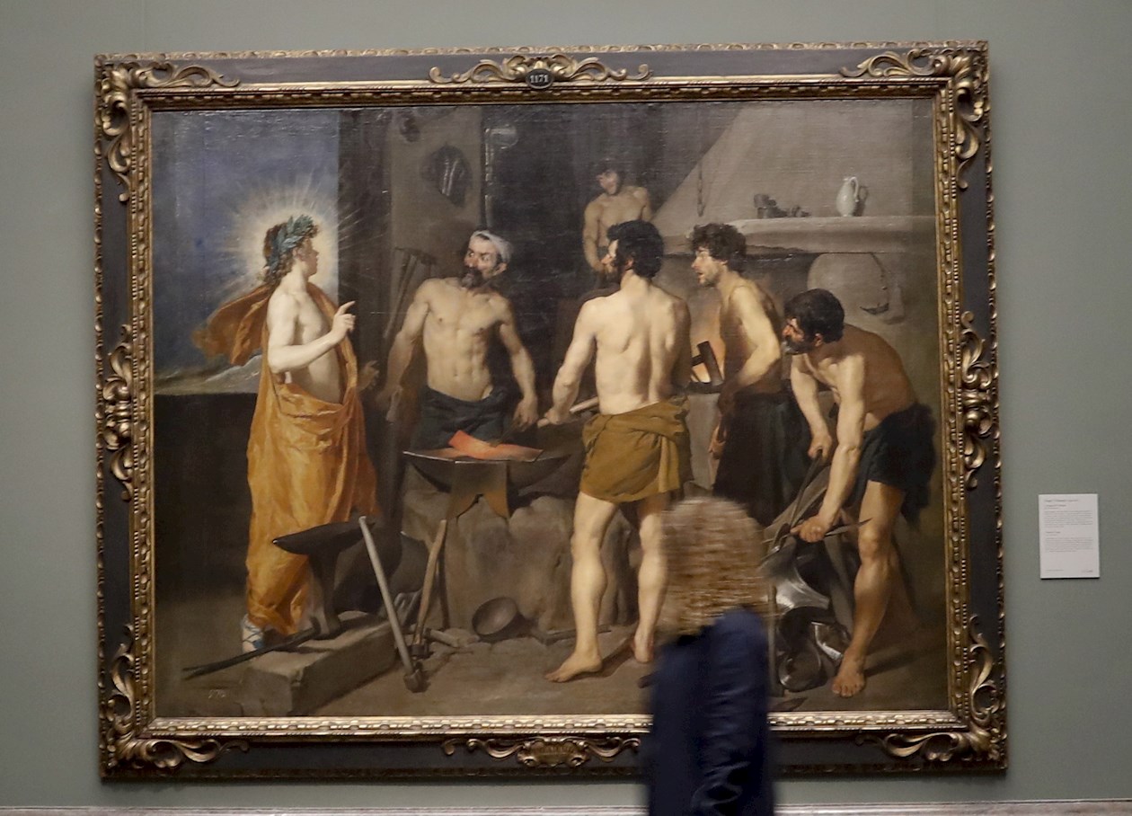 Una periodista pasa ante la obra 'La fragua de Vulcano', de Diego Velázquez, expuesta en la muestra "Reencuentro".