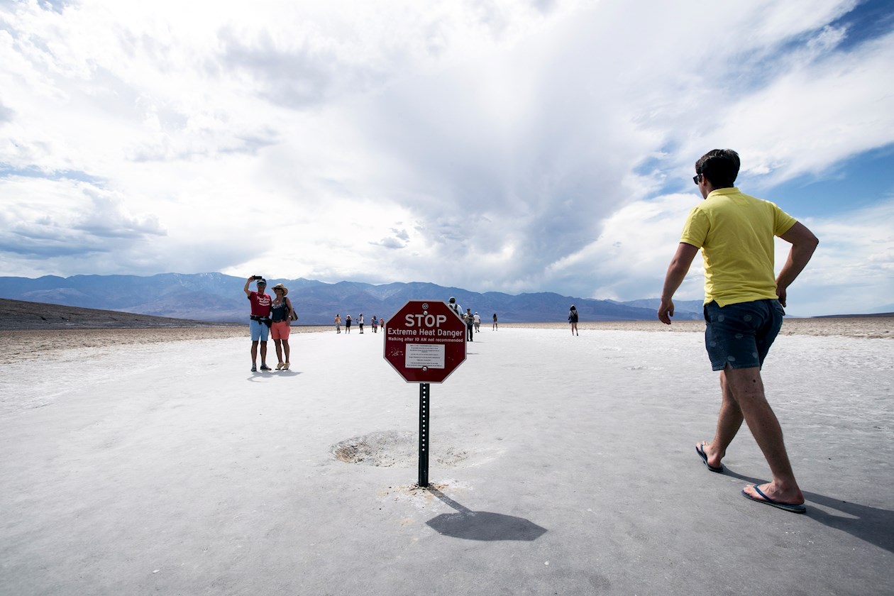 Los turistas caminan junto al letrero de advertencia de altas temperaturas en la cuenca de Badwater, ubicada a 855 metros por debajo del nivel del mar, en Death Valley, cerca de Furnace Creek, California, EE. UU.
