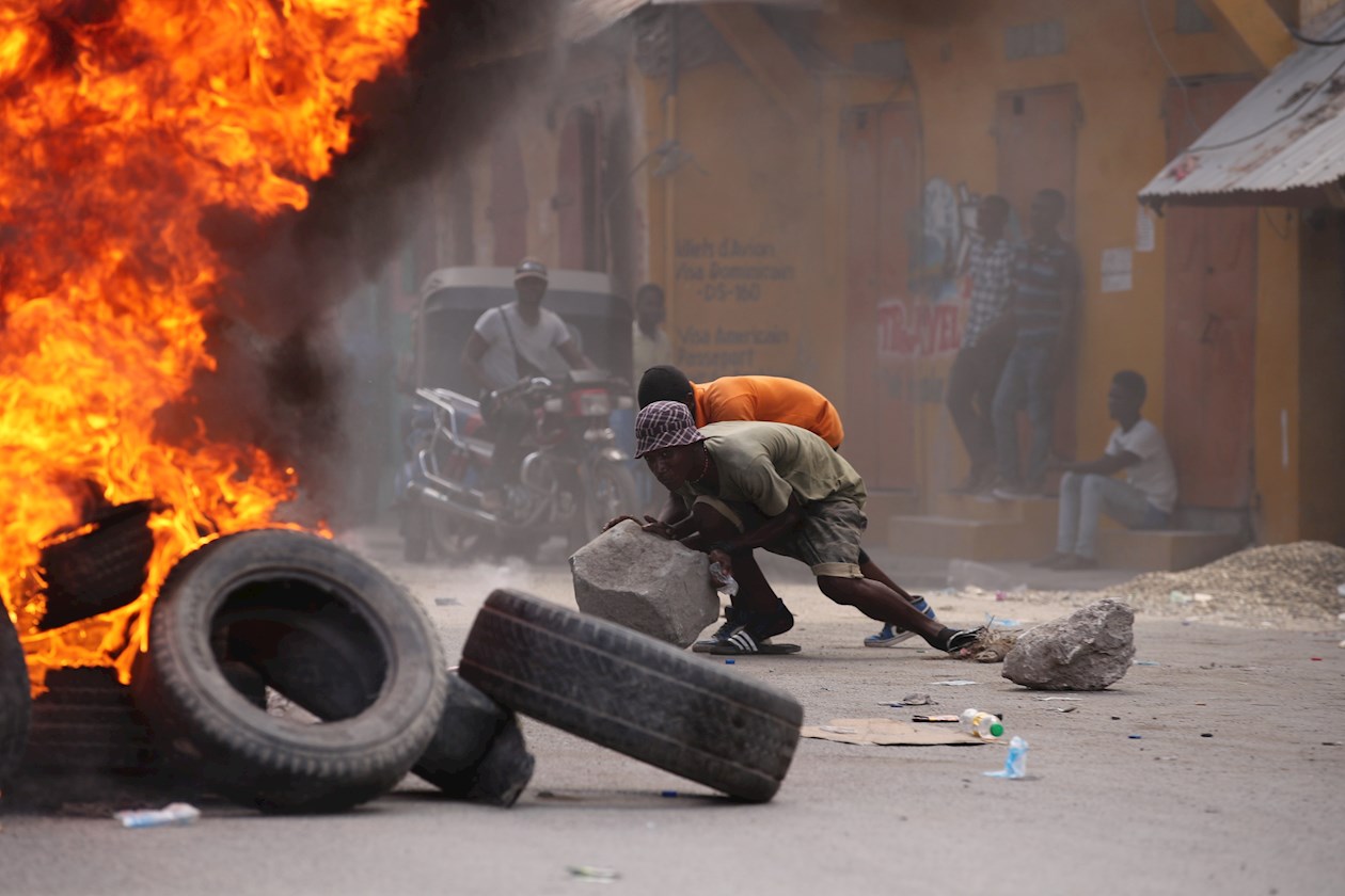 Dos hombres es visto cerca a una pila de llantas en llamas durante una jornada de protestas a la vez que se rindieron homenajes al asesinado presidente Jovenel Moise, hoy, en Cap-Haitien (Haití). 