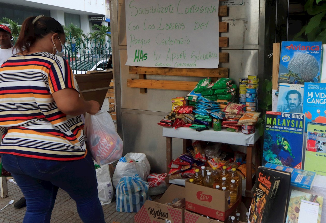 Una mujer entrega una bolsa con comida a cambio de libros en uno de los kioscos de los libreros del parque Centenario de Cartagena.
