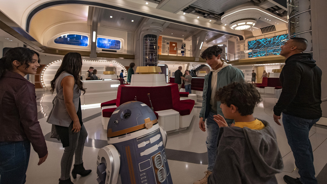 Un grupo de personas mientras son recibidos por el droide astromecánico SK-62O en el atrio del crucero estelar Halcyon, en el hotel atracción "Star Wars: Galactic Starcruiser" de Walt Disney World Resort en Lake Buena Vista, Florida (EE.UU.). 