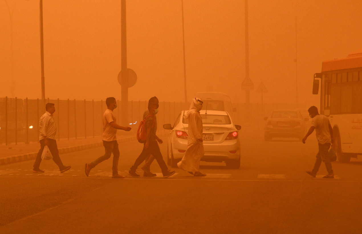 La gente camina en una calle envuelta en polvo pesado en la ciudad de Kuwait.