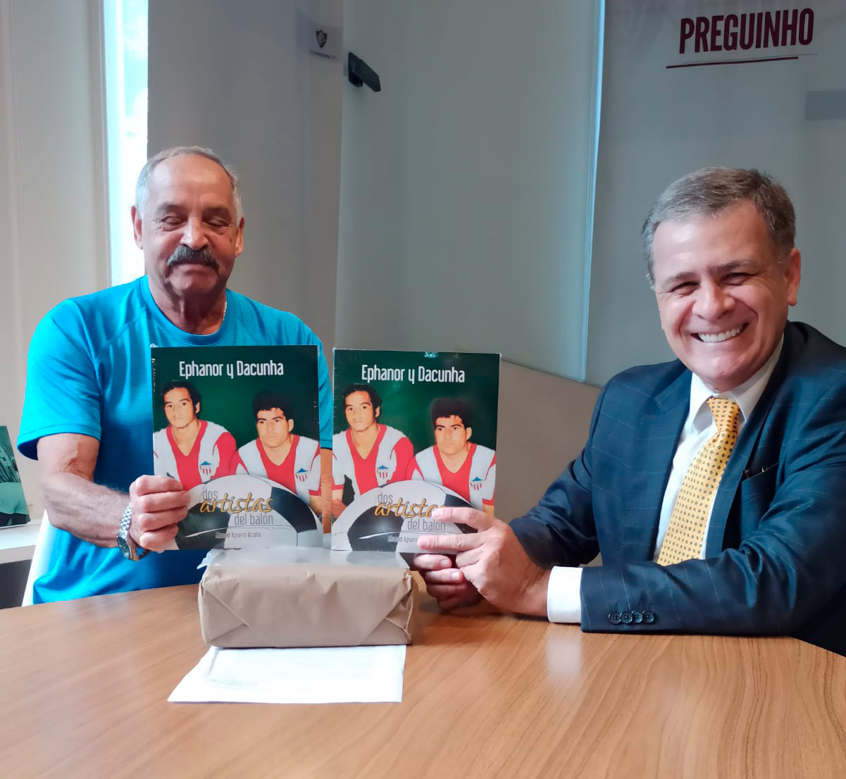Victor Ephanor con el delegado del Fluminense Marcelo Penha en la sede del club brasilero mostrando el libro en el que es el gran protagonista