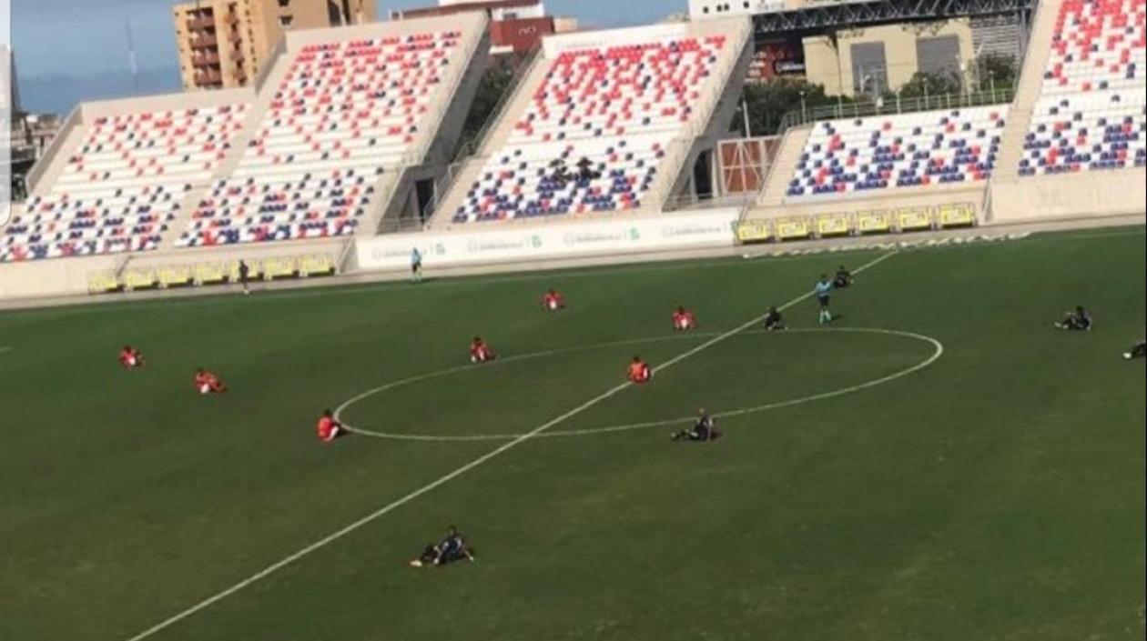 Jugadores del Barranquilla FC y del Deportivo Pereira se sientan en la cancha. 