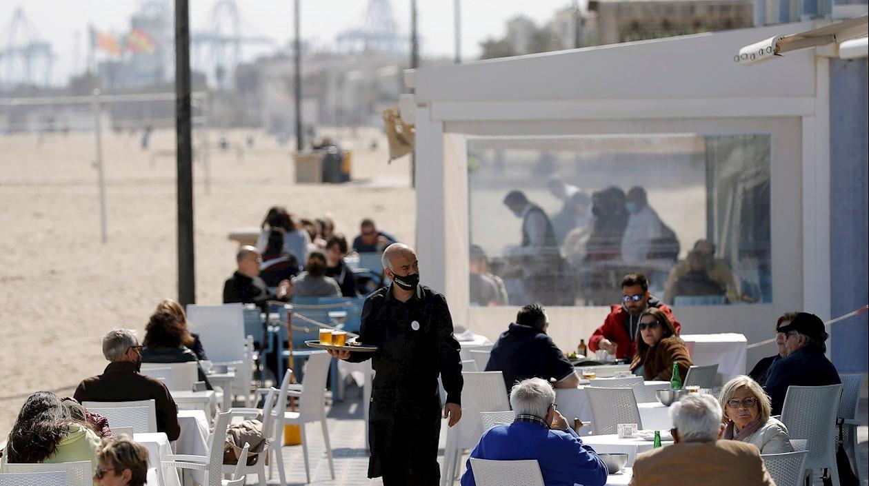 Un camarero atiende las mesas de una terraza en un restaurante en la playa.