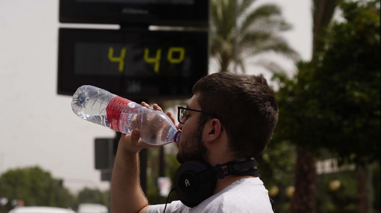 Un ciudadano bebe agua con el fondo de un termómetro que marca 44 grados.