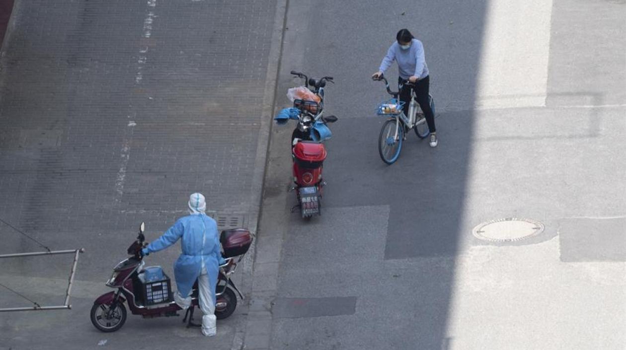 Un mensajero con equipo de protección personal y una mujer en bicicleta son vistos en Shanghai, China.