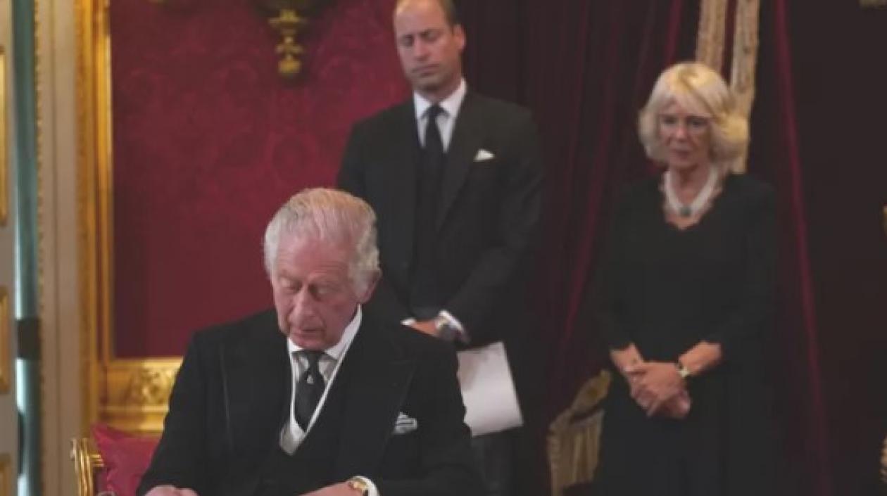 II firma el documento luego de juramentarse. A su lado la reina consorte, Camila, y el príncipe de Gales, Guillermo.