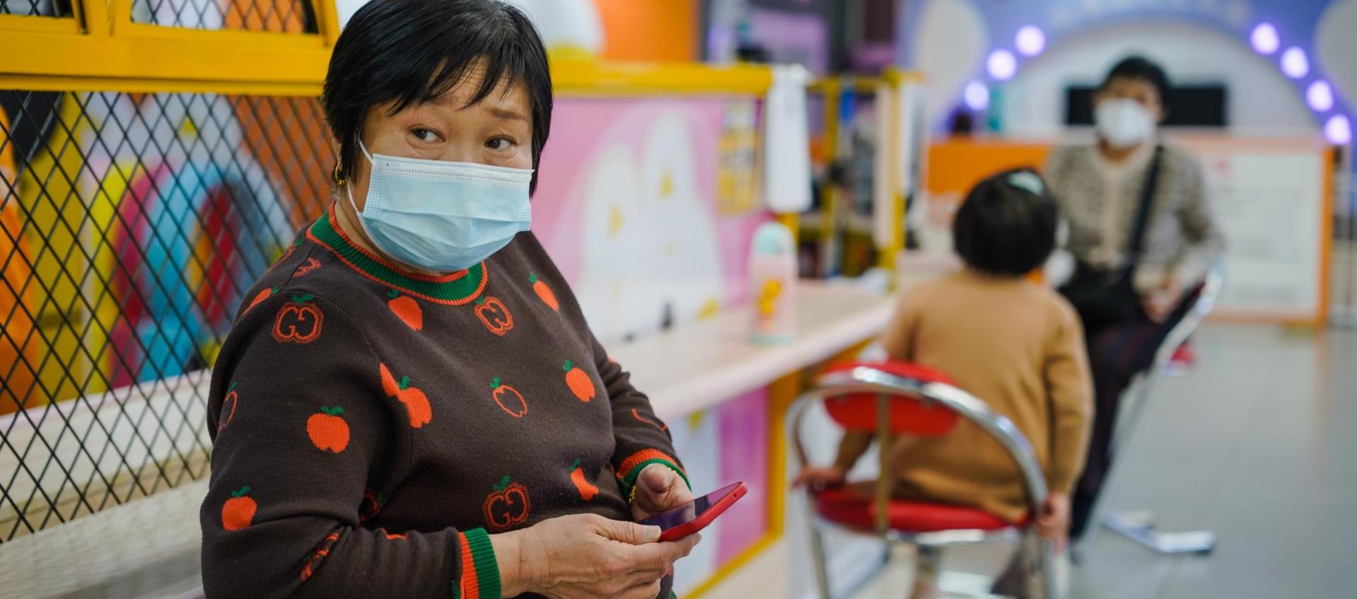 Una mujer protegida con una mascarilla utiliza su móvil en un centro comercial de Pekín.