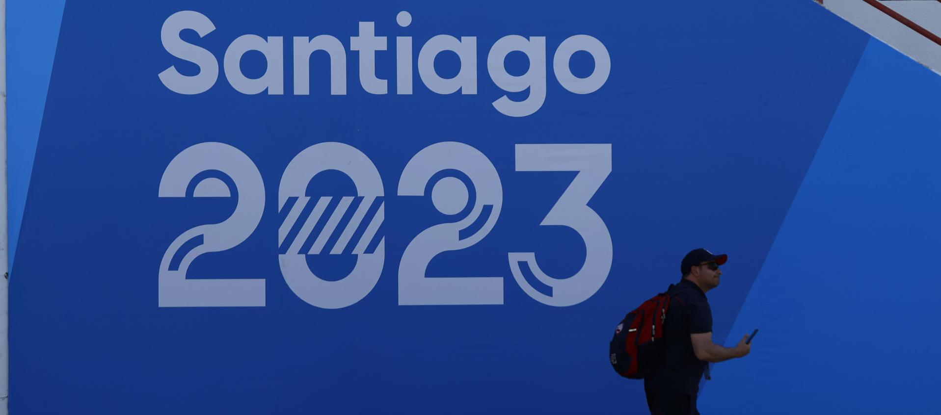 Un hombre camina frente a un cartel de Santiago 2023.
