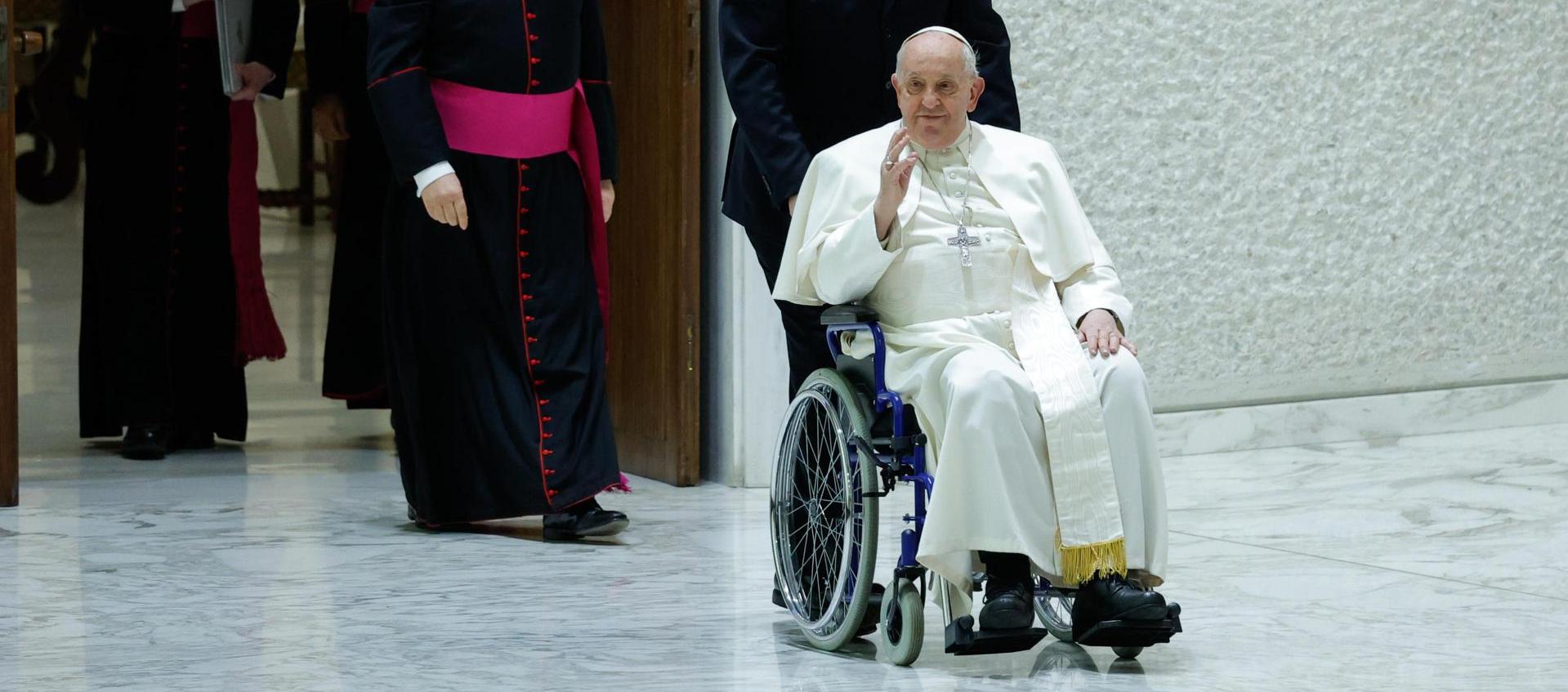 El papa Francisco saluda en silla de ruedas a su llegada al Aula Pablo VI.