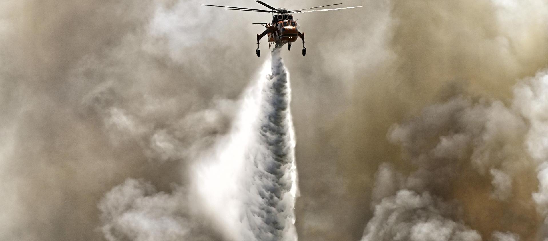 Un helicóptero de extinción de incendios arroja agua durante un incendio forestal. 