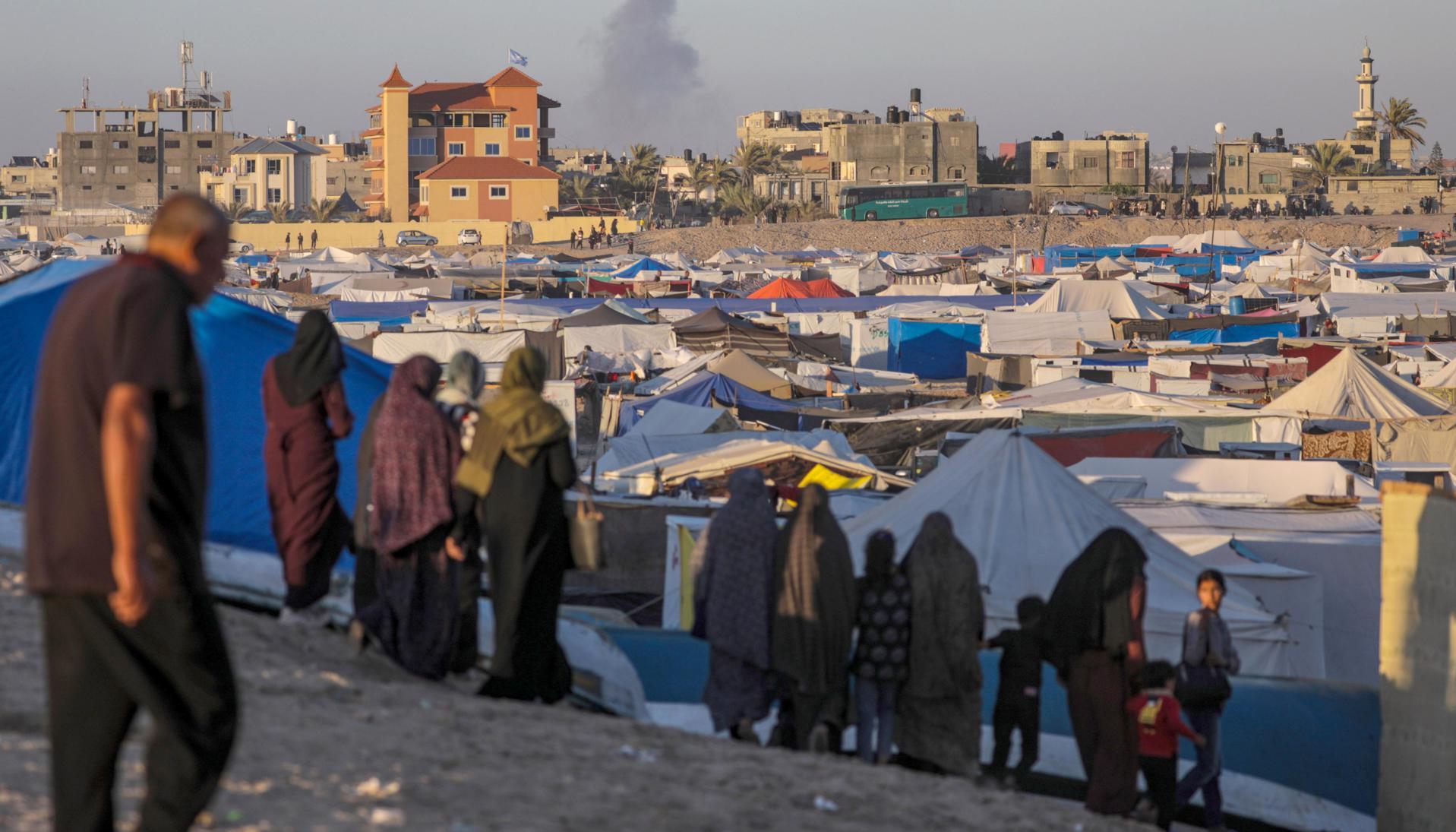 Desplazados internos palestinos y al fondo tras un ataque aéreo israelí en Rafah.