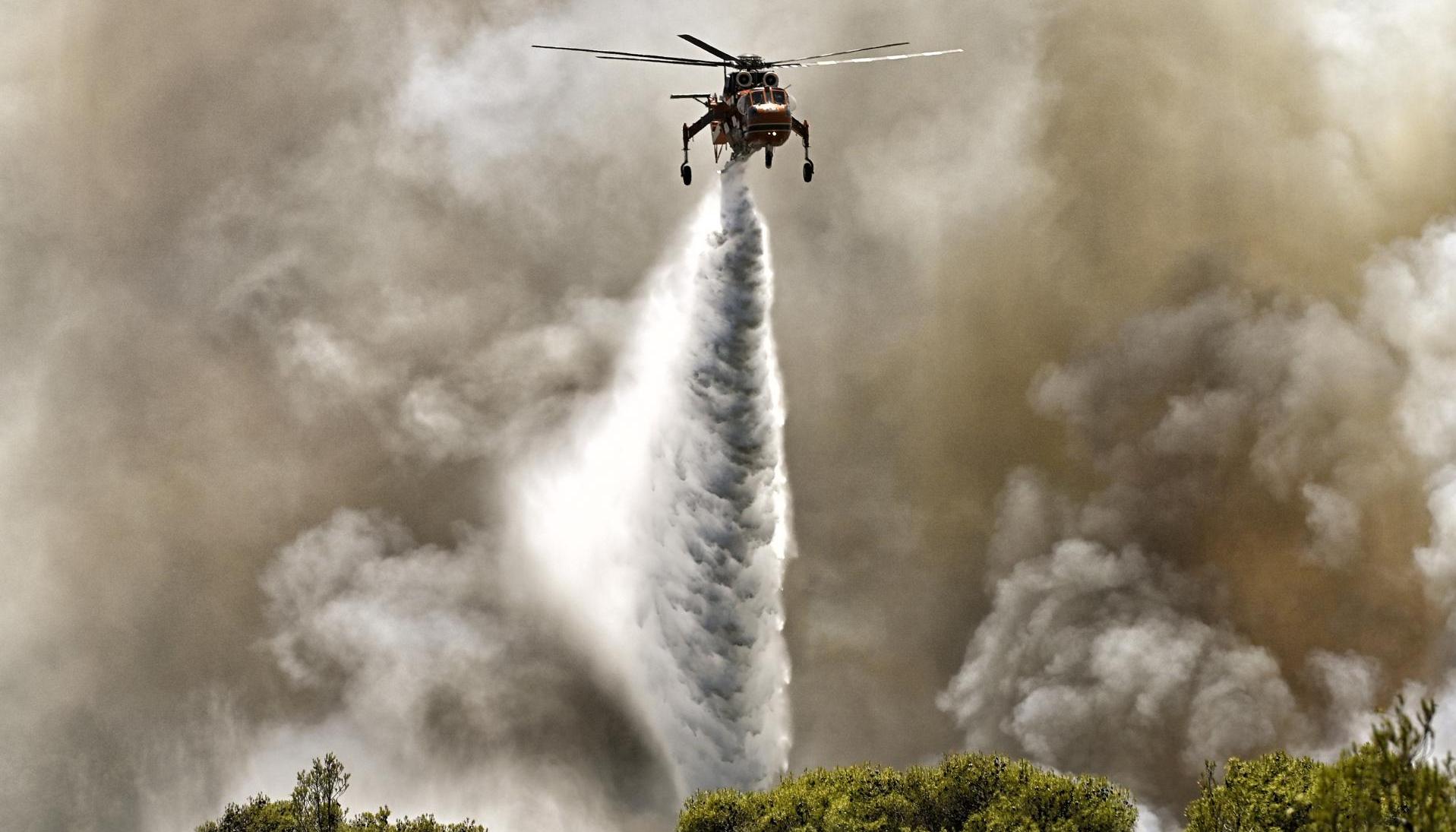 Un helicóptero de extinción de incendios arroja agua durante un incendio forestal. 