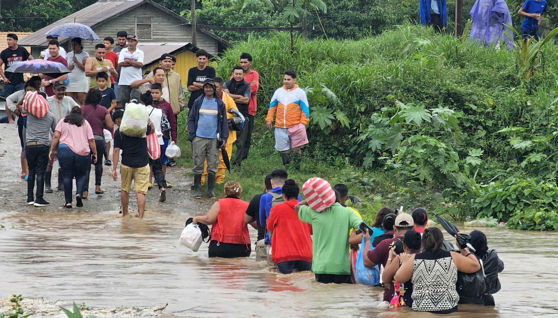 Comunidad cruzando con sus pertenencias por un río en medio de las inundaciones.