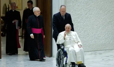 El papa Francisco saluda en silla de ruedas a su llegada al Aula Pablo VI.
